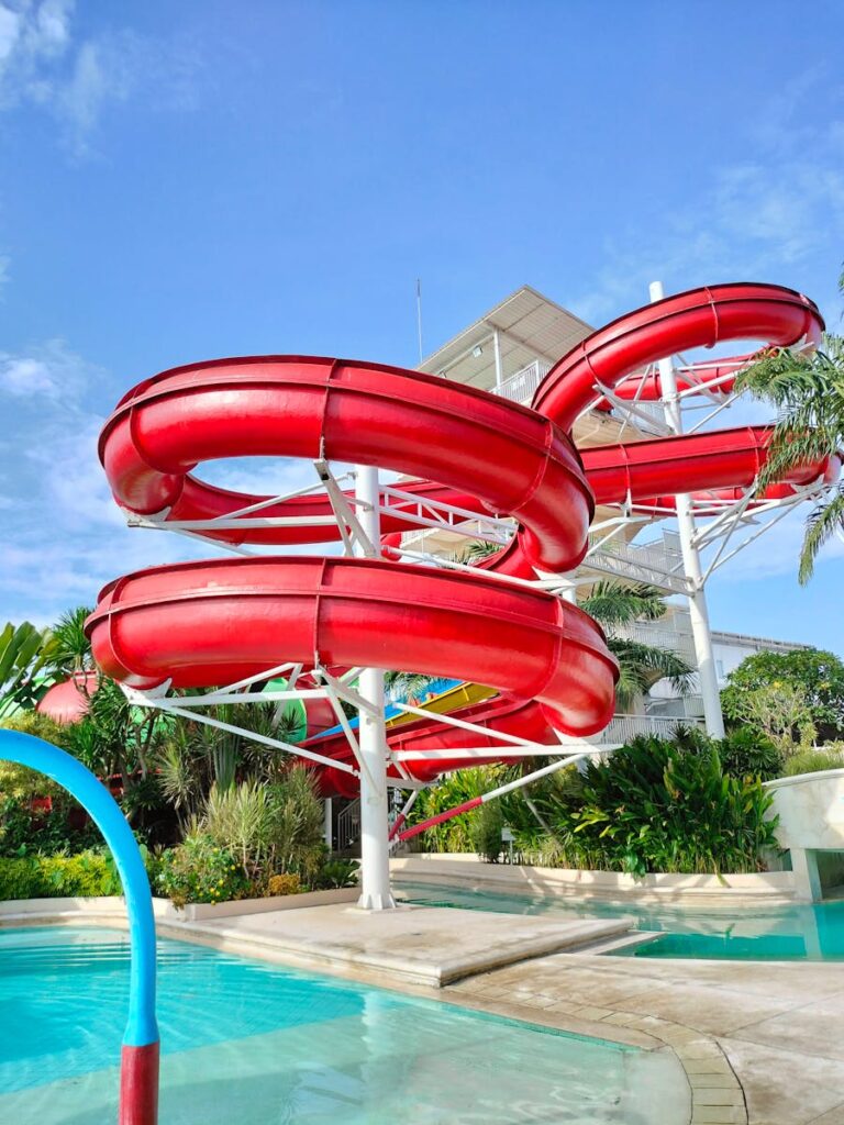 Red water slides in a tropical waterpark under a clear blue sky.